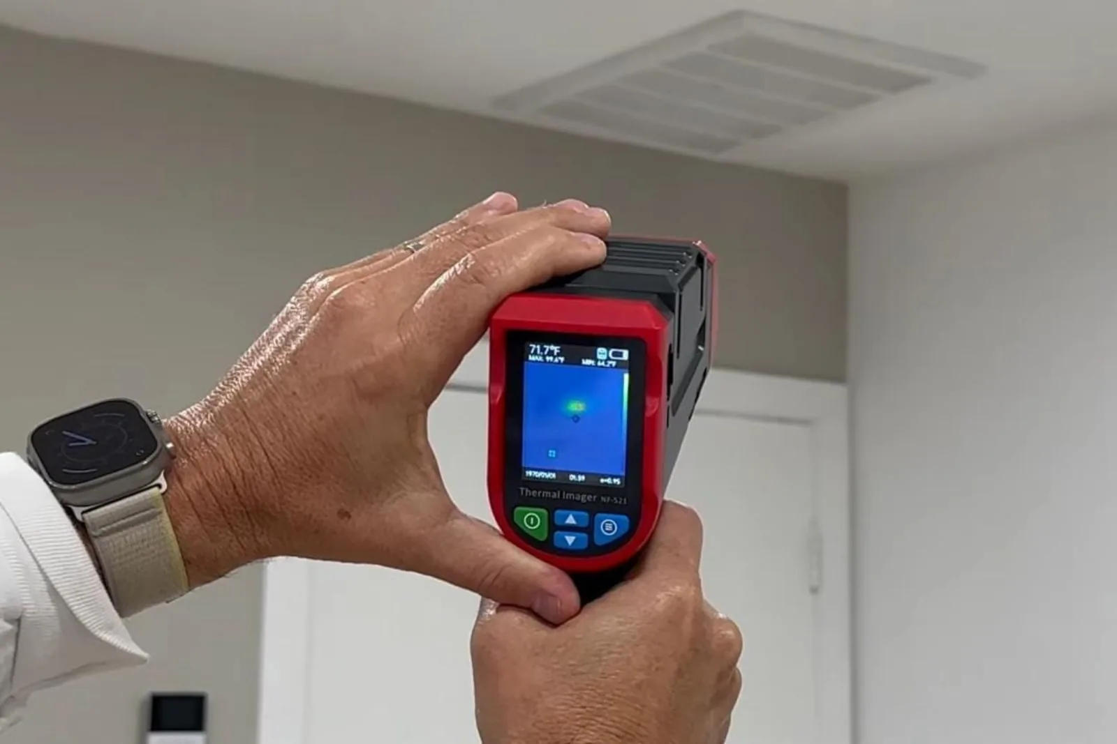 Hands holding a thermal imaging camera to scan a wall for a hidden leak