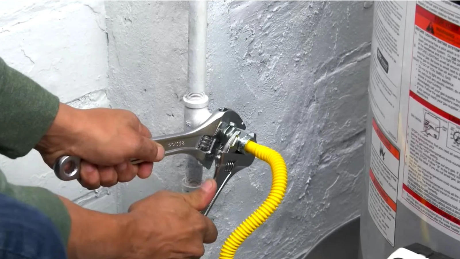 Wrench tightening a yellow gas flex connector on a water heater
